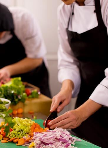 Team cooking Milano-Como: dettaglio mani di cuochi che tagliano verdure
